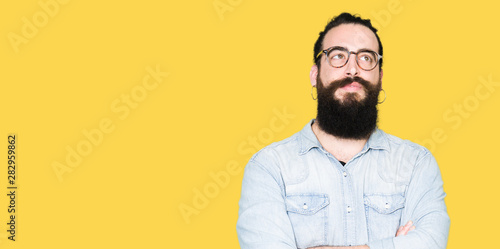 Young hipster man with long hair and beard wearing glasses smiling looking side and staring away thinking.