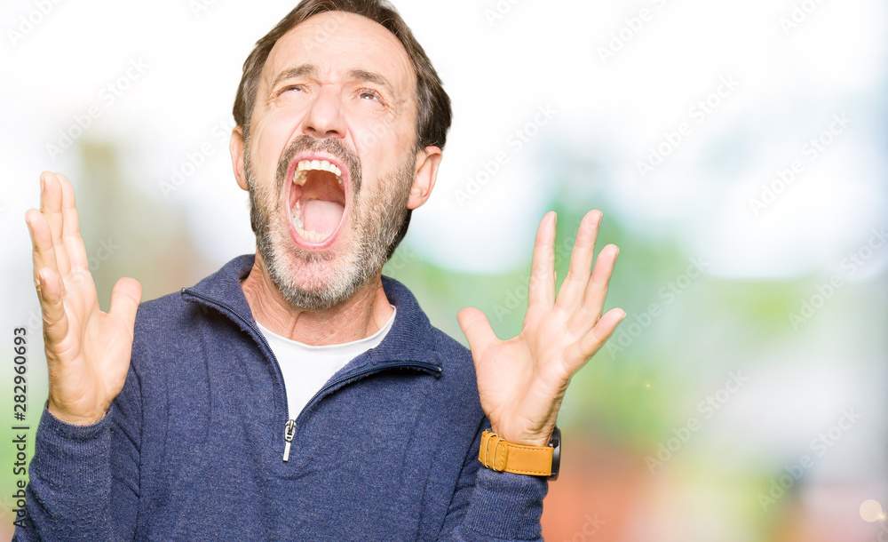 Middle age handsome man wearing a sweater crazy and mad shouting and yelling with aggressive expression and arms raised. Frustration concept. Middle age handsome man wearing a sweater crazy and mad shouting and yelling with aggressive expression and arms raised. Frustration concept.