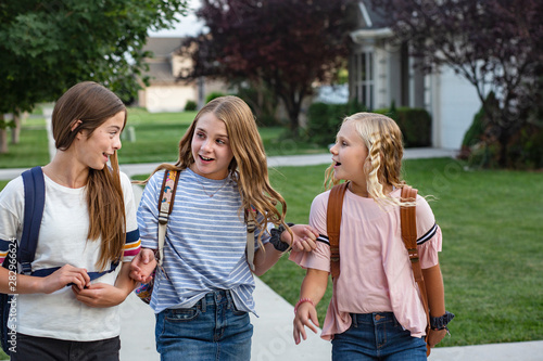 Group of young female friends and students talking together as they walk home school for the day