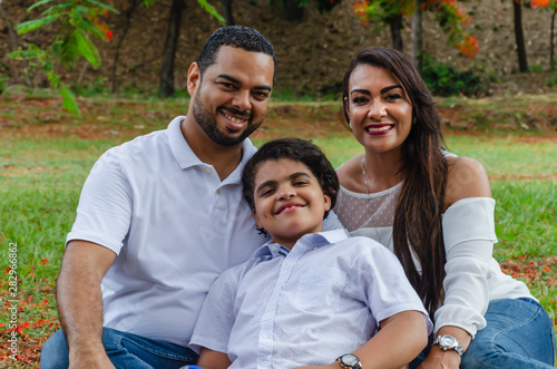 couple of Latin American men and women, with boy suffers autism, happy in a portrait family outdoors together in a park, the three laughing hugging