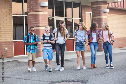 Large, diverse group of kids leaving school at the end of the day. School friends walking together and talking together on their way home