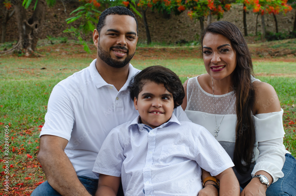 couple of Latin American men and women, with boy suffers autism, happy in a portrait family outdoors together in a park, the three laughing hugging couple of Latin American men and women, with boy suffers autism, happy in a portrait family outdoors together in a park, the three laughing hugging