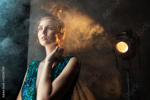 Charning woman in spotlight beam and smoke looking into the distance