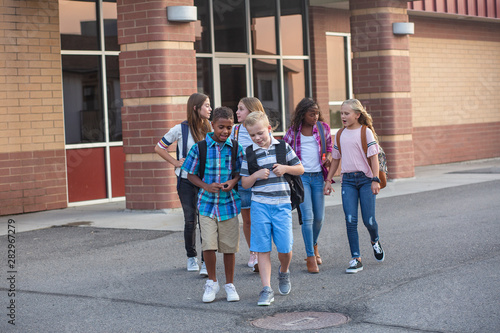 Large, diverse group of kids leaving school at the end of the day. School friends walking together and talking together on their way home photo