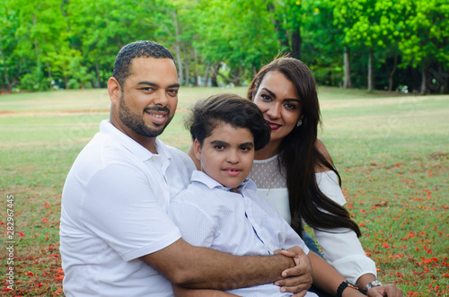 couple of Latin American men and women, with boy suffers autism, happy in a portrait family outdoors together in a park, the three laughing hugging © Francisco