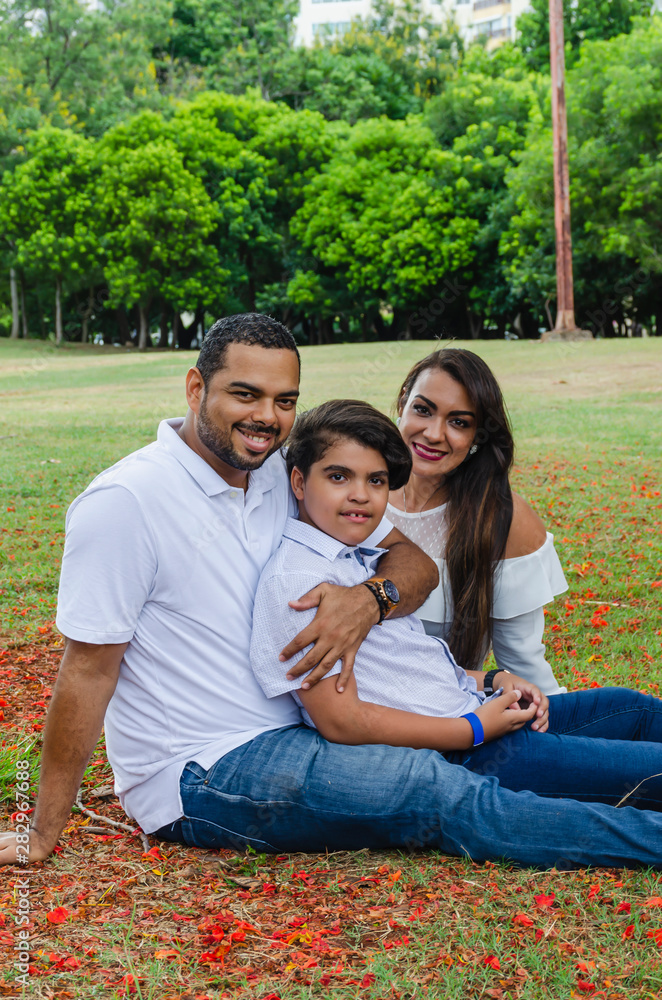 couple of Latin American men and women, with boy suffers autism, happy in a portrait family outdoors together in a park, the three laughing hugging couple of Latin American men and women, with boy suffers autism, happy in a portrait family outdoors together in a park, the three laughing hugging