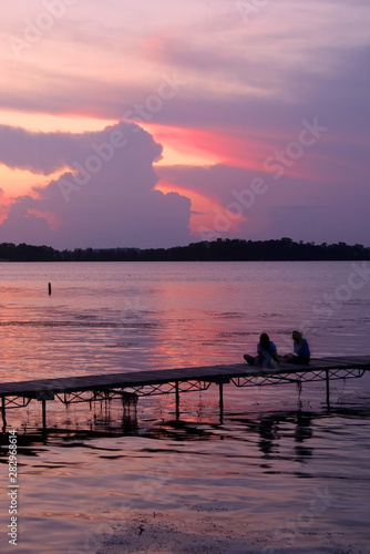 Beautiful summer landscape with colorful after sunset sky.Scenic view with bright color sky reflects in a lake and two silhouettes on a wooden pier enjoying sunset over lake Mendota. Madison  WI  USA.