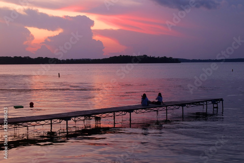 Beautiful summer landscape with colorful after sunset sky.Scenic view with bright color sky reflects in a lake and two silhouettes on a wooden pier enjoying sunset over lake Mendota. Madison, WI, USA.