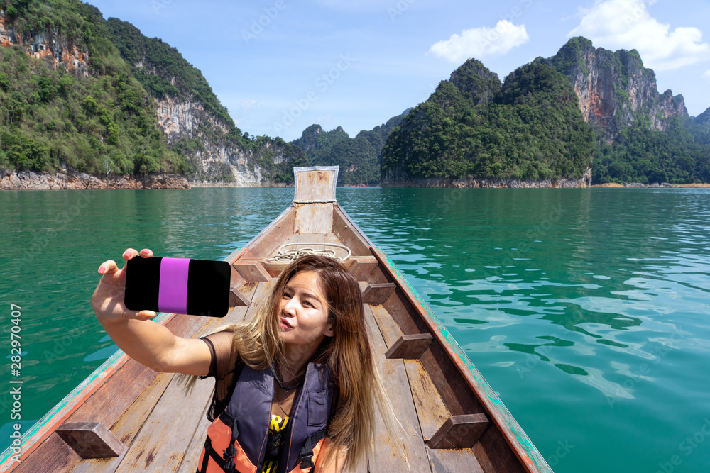 Asian woman taking selfie on wooden boat with mountains background Asian woman taking selfie on wooden boat with mountains background