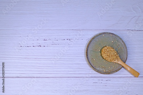 Wooden spoon full of quinoa on ceramic plate on white wooden background with space on the left. 