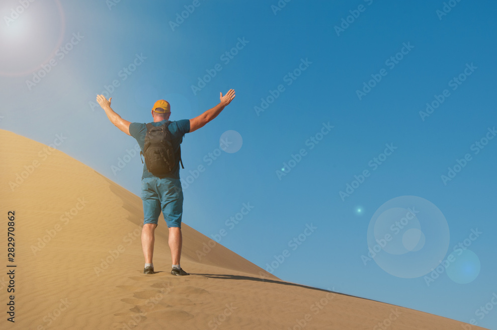 A man with backpack on the sand dune happy to be there. Male rise his hands in desert landscape A man with backpack on the sand dune happy to be there. Male rise his hands in desert landscape
