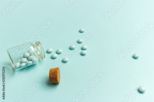 Canvas Print Glass bottle with pills scattered on a turquoise background