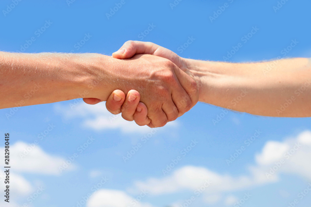 Men is handshake against the background of clouds and the blue sky. Image businessmans handshake. Men is handshake against the background of clouds and the blue sky. Image businessmans handshake.