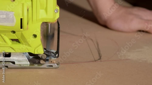 Close-up of electric jigsaw in action, men's hand cutting up wood board with a jigsaw in 4K photo