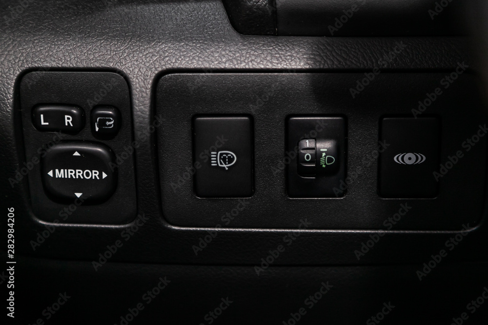 Close-up on the headlight, side mirror switch control buttons, automatic adjust level dashboard. modern car interior: parts, buttons, knobs. Close-up on the headlight, side mirror switch control buttons, automatic adjust level dashboard. modern car interior: parts, buttons, knobs.
