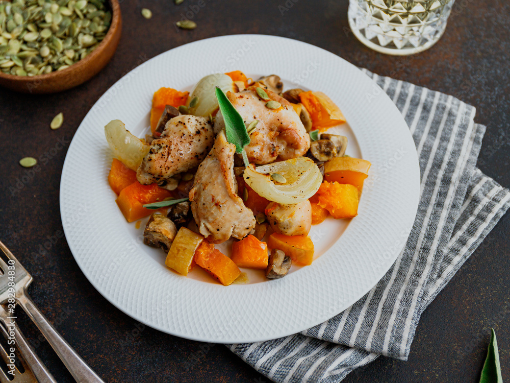 Seasonal autumn low calorie recipe from baked turkey medallions with pumpkin, onion, shampinions and sage on a white plate.