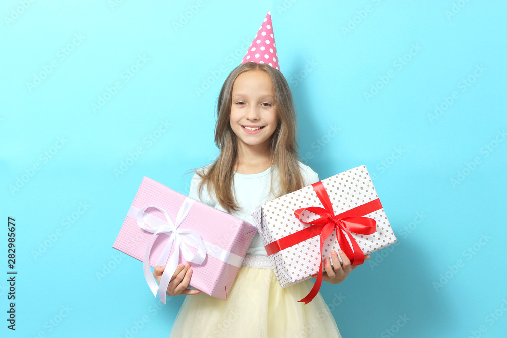 Portrait of a little girl in a festive cap and with a gift in her hands on a colored background. Birthday, presents, holiday Portrait of a little girl in a festive cap and with a gift in her hands on a colored background. Birthday, presents, holiday
