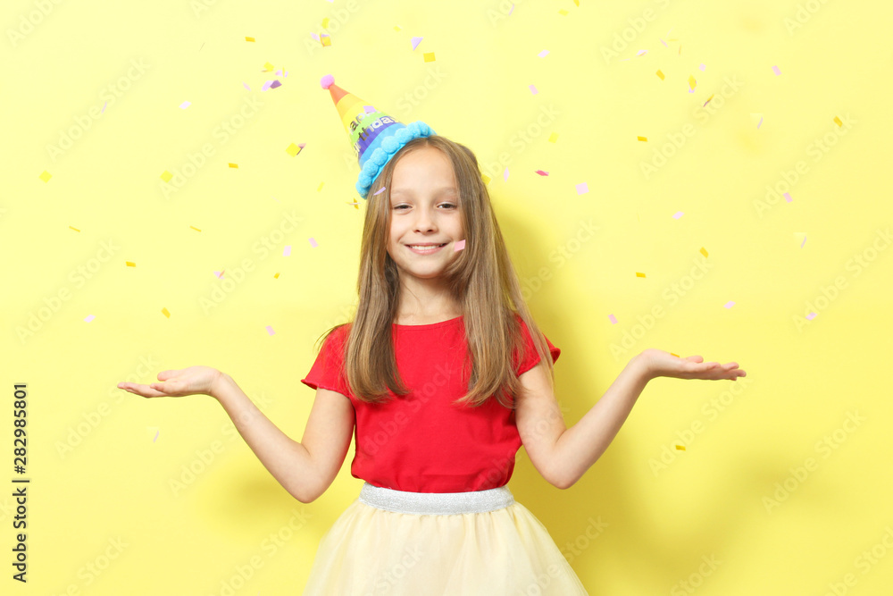 Portrait of a little girl in a festive cap on a colored background and confetti.