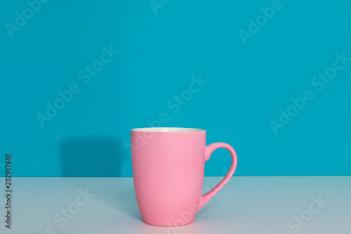 Pink cup on light surface on bright blue background
