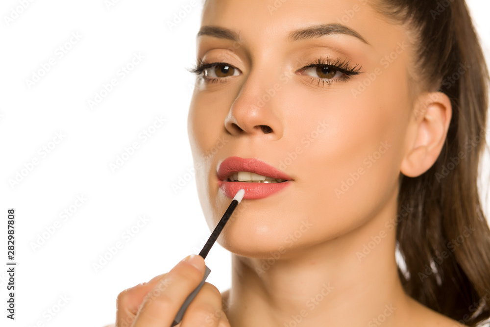 young beautiful woman applying lipgloss on white background