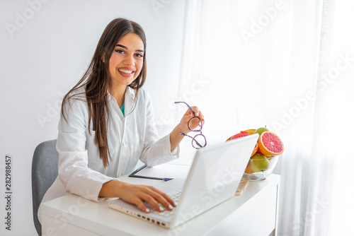 Portrait of young smiling female nutritionist in the consultation room. Portrait of beautiful smiling nutritionist looking at camera and showing healthy vegetables in the consultation. photo