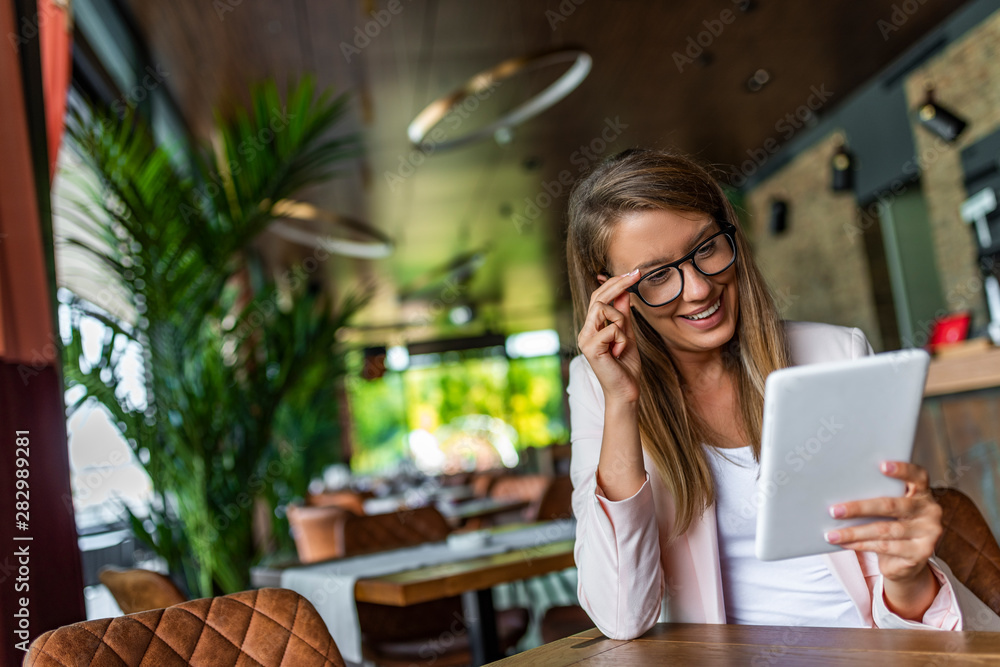 Pretty young female manager using modern digital tablet at cafe, smiling girl working at cafe via tablet pc, attractive businesswoman sitting at vintage loft during a break Pretty young female manager using modern digital tablet at cafe, smiling girl working at cafe via tablet pc, attractive businesswoman sitting at vintage loft during a break