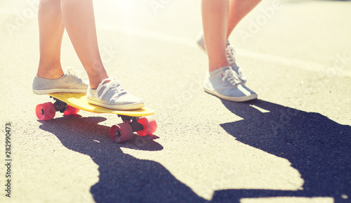 summer, extreme sport and people concept - feet of teenage couple riding short modern cruiser skateboard on road