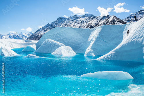 Climber ascending a large wall of ice over a blue glacial lake on the Matanuska Glacier.