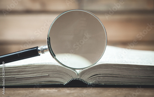 Magnifying glass with book on a wooden table. Search and discover