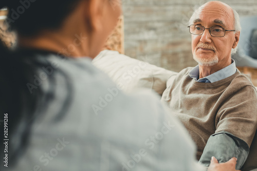 Wise senior directly looking on his doctor while she working with him