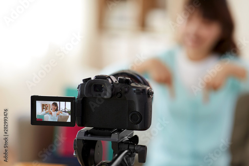 blogging, technology, videoblog and shopping concept - camera recording video blog of happy smiling asian woman or blogger pointing fingers downwards at home © Syda Productions
