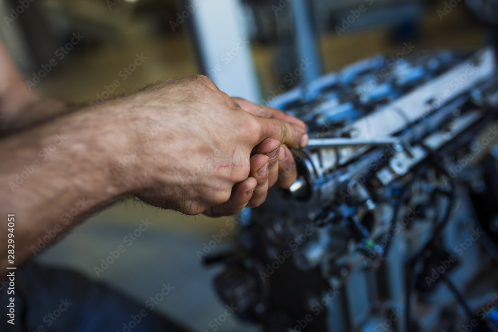 Mechanic with a tool in his hands repairing the motor of the machine. The process of working in the service station Mechanic with a tool in his hands repairing the motor of the machine. The process of working in the service station