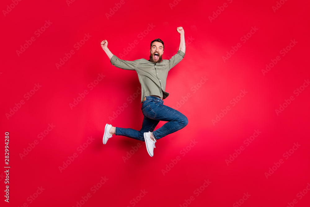 Full length body photo of turned rejoicing man jumping with happiness seeing his team winning contests while isolated with red background