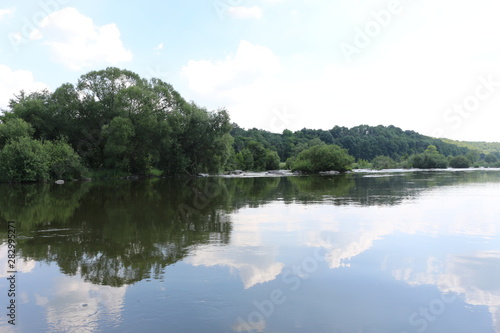 Clouds are reflected in the river. Sunny windless weather. Peace and silence. Natural beauty.