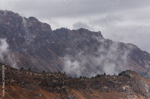 Photo of mountains with trees, smoke, gray sky