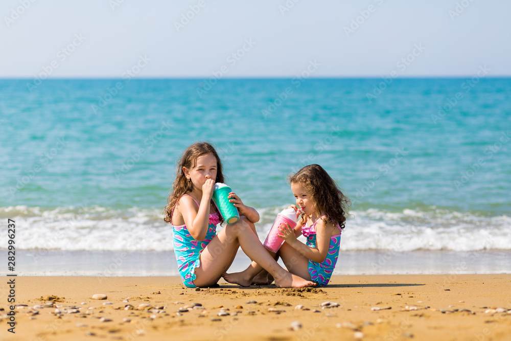 little girls sit sit opposite each other and drink from colored beautiful cocktail glasses Family vacation concept little girls sit sit opposite each other and drink from colored beautiful cocktail glasses Family vacation concept