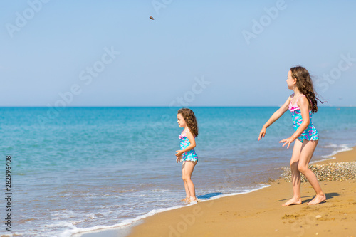 little girls in bright swimsuits play on the beach. Children on vacation. Family vacation. happy sisters