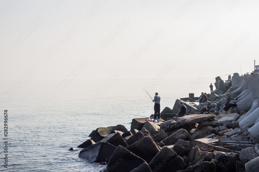 Men fishing on rocks by the sea.