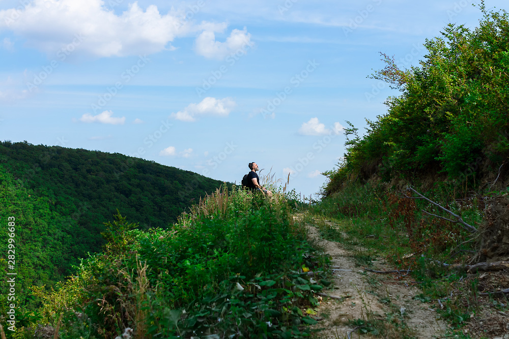 Fototapeta premium Top of the hill, trail leading to the top and one lonely male figure sitting and relaxing after the hike