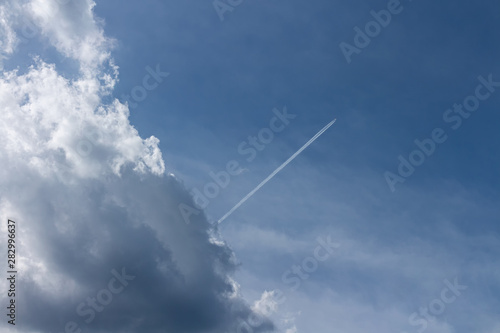 Bright blue sky with backlit cloud and an airplane shooting thru it