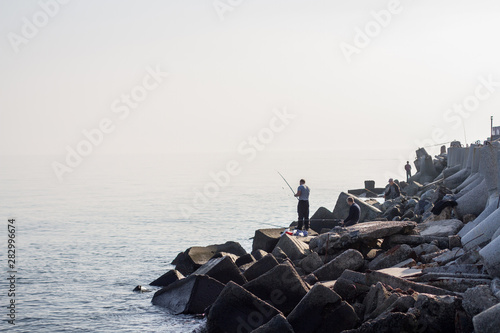 Men fishing on rocks by the sea.
