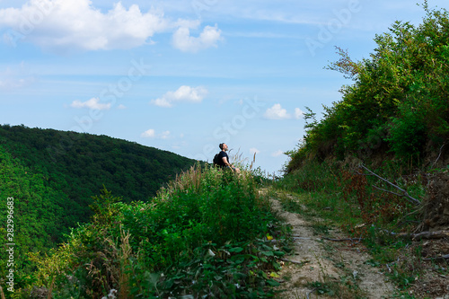 Top of the hill, trail leading to the top and one lonely male figure sitting and relaxing after the hike