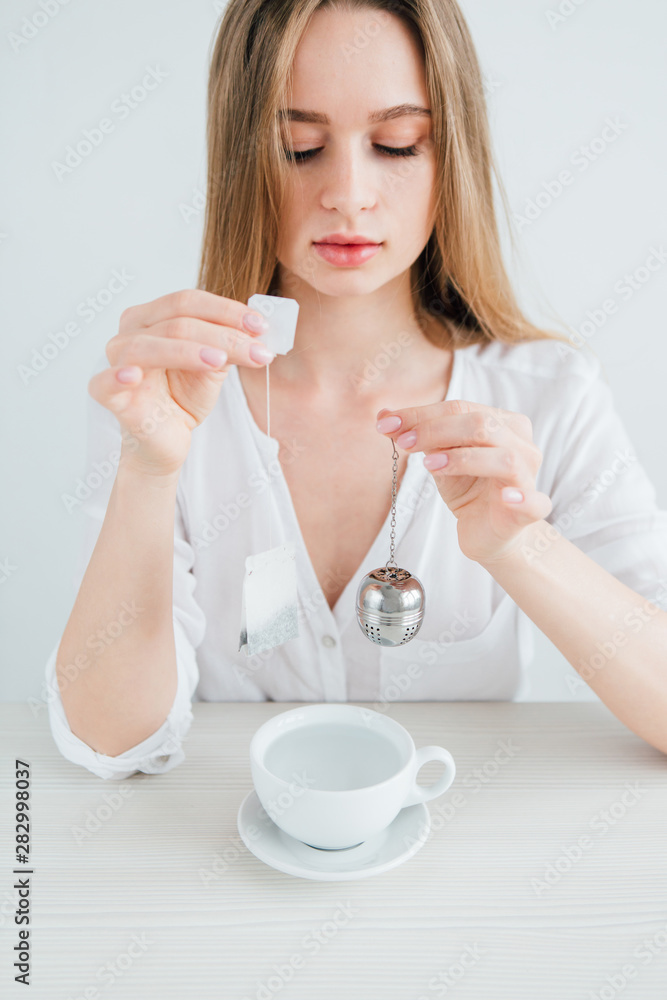 Girl compares a useful reusable metal tea strainer with a harmful tea bag Girl compares a useful reusable metal tea strainer with a harmful tea bag