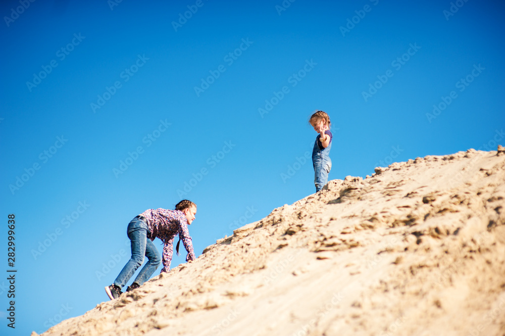 Girl crawls up the mountain of sand to the second girl