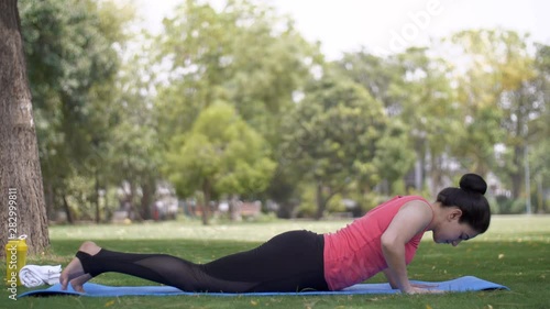 Beautiful young woman doing yoga postures on a fitness mat in a garden - sportswear. Pretty Indian lady performing Bhekasana or frog posture with all her concentration under a tree on a yoga mat - ... photo