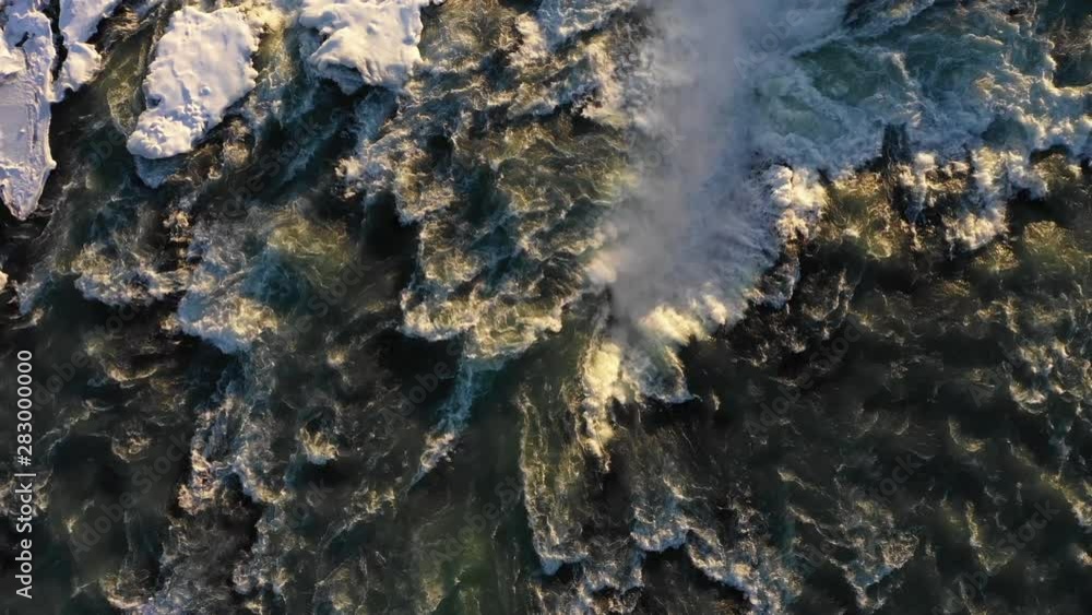 Overhead drone shot flying over powerful waterfall with snow and ice, natural landscapes popular travel destination Iceland Overhead drone shot flying over powerful waterfall with snow and ice, natural landscapes popular travel destination Iceland