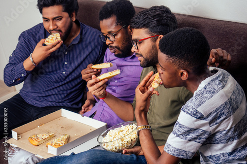 Wallpaper Mural four african american males eating pizza at home party,throwing popcorn into each other Torontodigital.ca