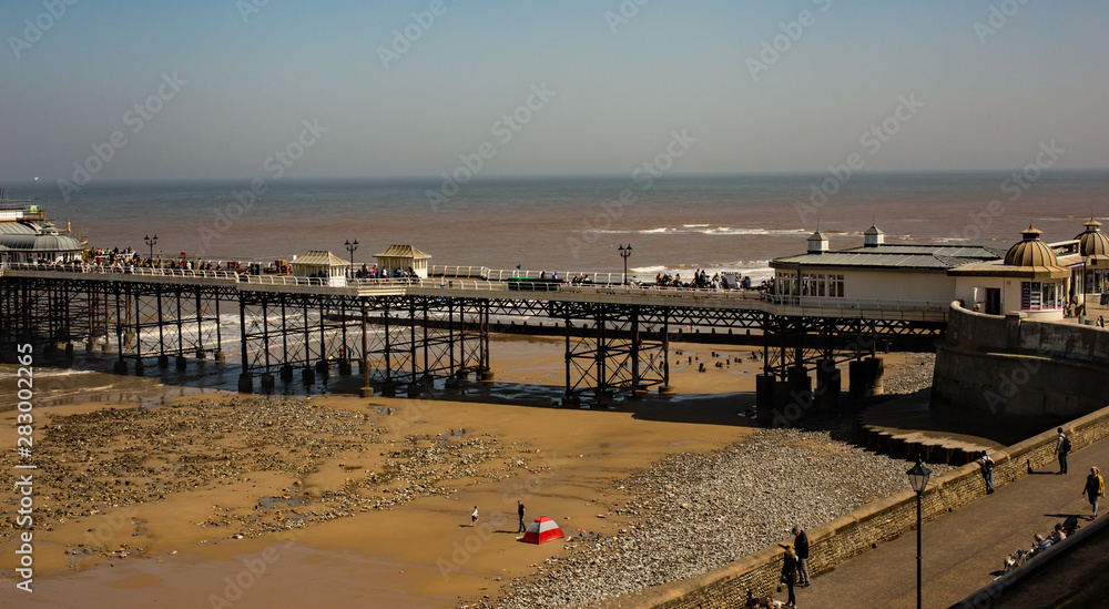 A high up view of the sea front promenade and first part of Cromer pier, Norfolk. UK weather: A bright and sunny, but breezy day, with bright blue skies and light stratus clouds.