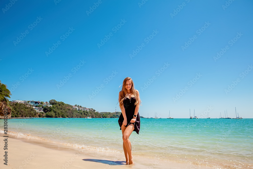 Beautiful young woman with long hair in a black dress standing near the sea and relax on the beach on Phuket, Thailand