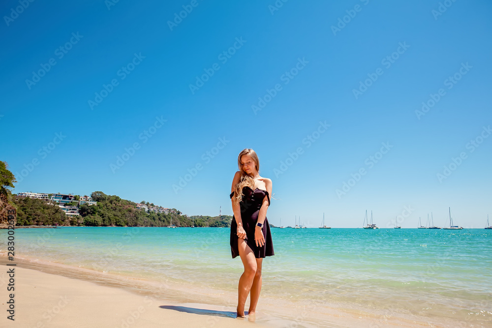 Beautiful young woman with long hair in a black dress standing near the sea and relax on the beach on Phuket, Thailand Beautiful young woman with long hair in a black dress standing near the sea and relax on the beach on Phuket, Thailand